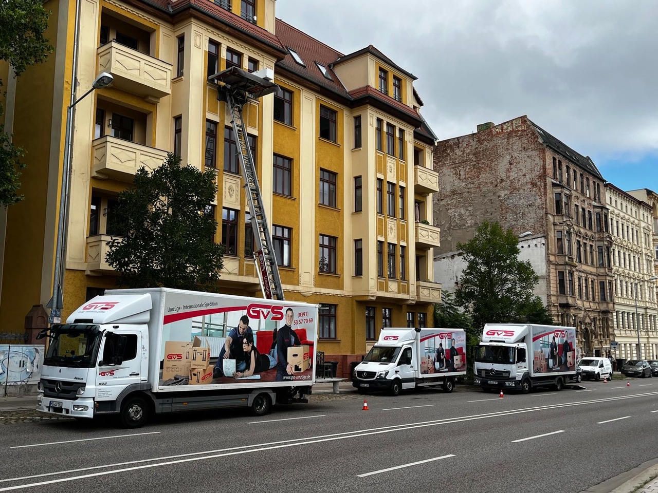 Drei GVS-Umzugsfahrzeuge und ein Möbellift im Einsatz an einer Häuserzeile